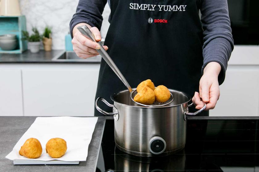 Arancini werden aus einem Topf gehoben.