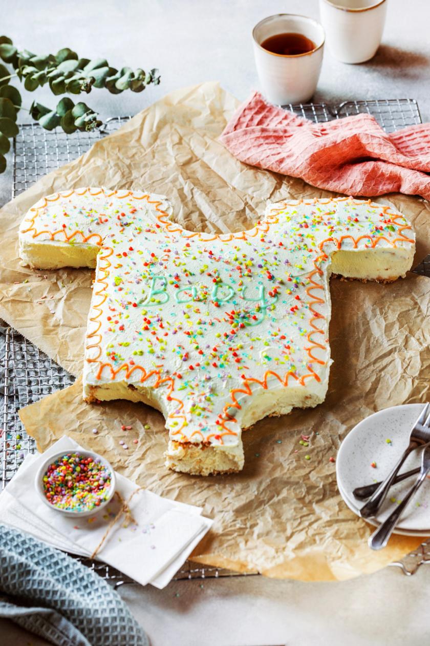 Bunt dekorierte Babyparty Torte in Form eines Babybodys auf einem Kuchengitter, daneben Streusel und Zuckerschrift