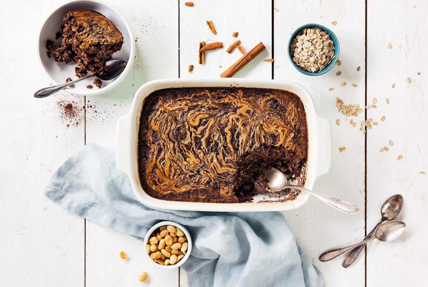 Baked Oatmeal auf einem Tisch. Drumherum Nüsse, Haferflocken.