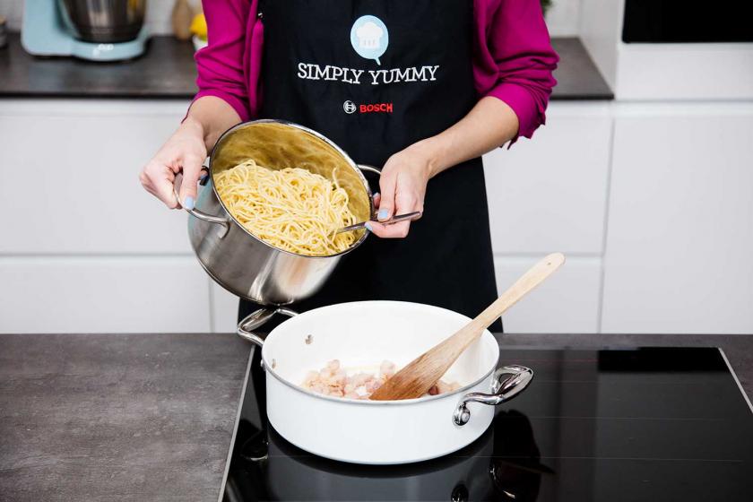Spaghetti für die Carbonara werden in der Pfanne verrührt.