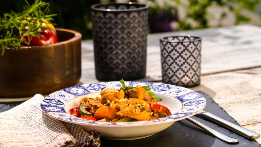 Curryreis mit Hähnchen und Gemüse im tiefen Teller auf dem Gartentisch.
