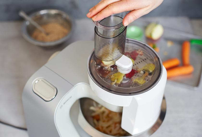 Möhren und ein Apfel werden in einer Küchenmaschine für die Overnight Oats mit Möhren geraspelt.