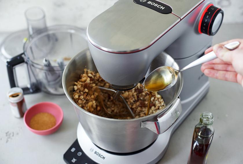 Ahornsirup wird zu Granola mit Nüssen in einer Küchenmaschine gegeben.