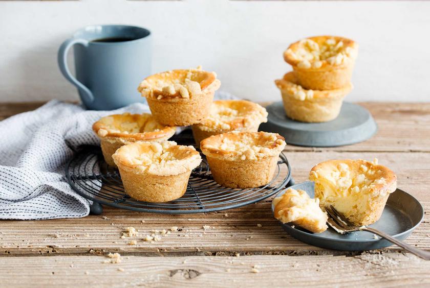 Mehrere Käsekuchemuffins mit Streuseln stehen auf einem Kuchengitter und auf einem Teller.