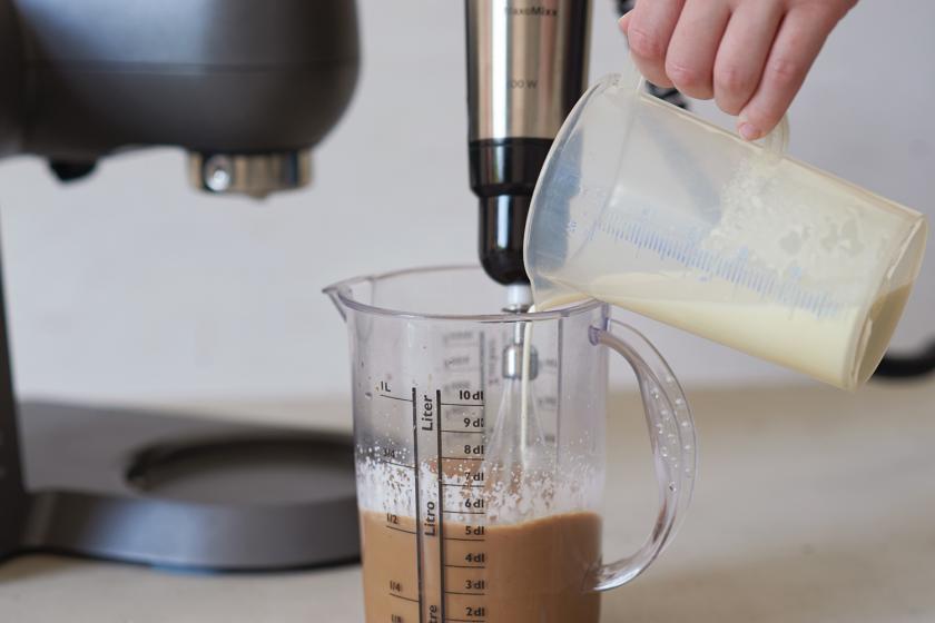 Sahne wird zu kaltem Kaffee in einem Messbecher gefüllt.