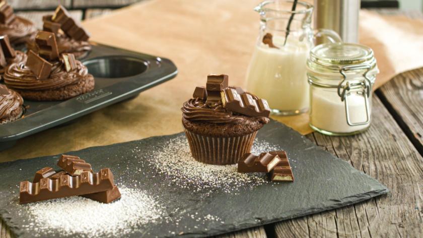 Kinderschokolade Cupcakes im Vordergrund mit weiteren Cupcakes im Hintergrund auf Schieferplatte.