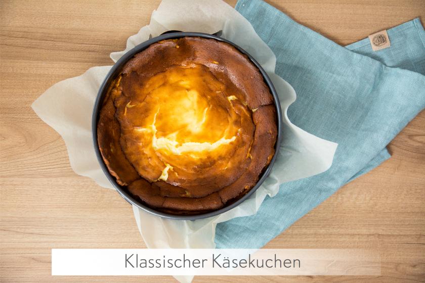 Ein ganzer Käsekuchen ohne Boden steht mit Form auf einem Tuch.