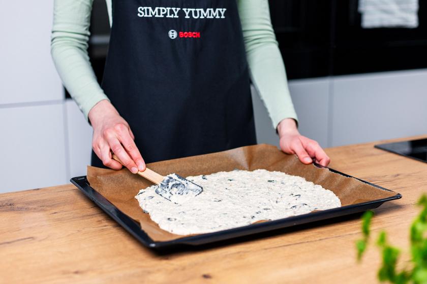 Teigmasse für das Knäckebrot wird auf einem Backblech verteilt.