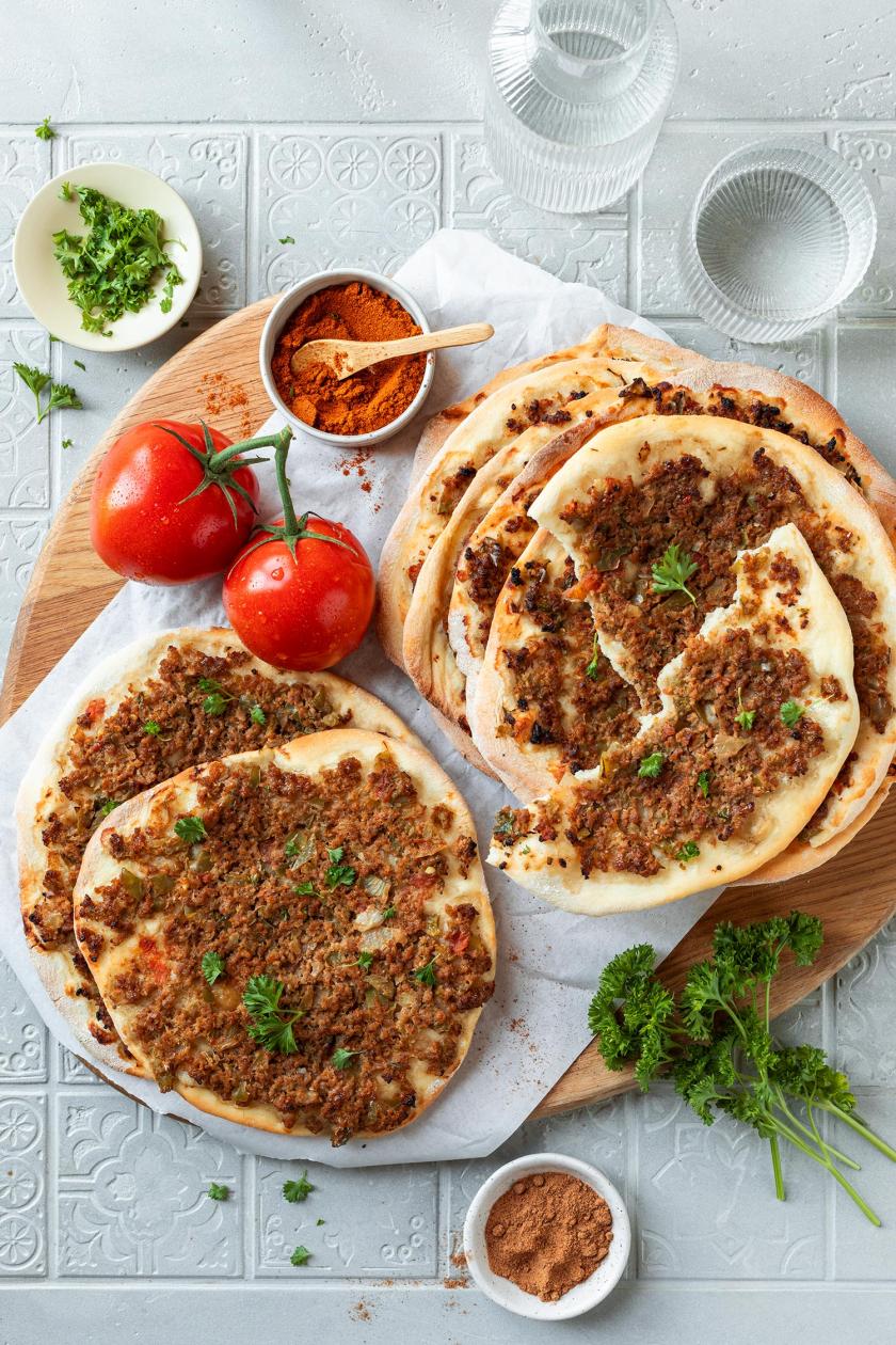 Mehrere Lahmacuns gestapelt auf einem Teller, daneben Tomaten und Gewürze