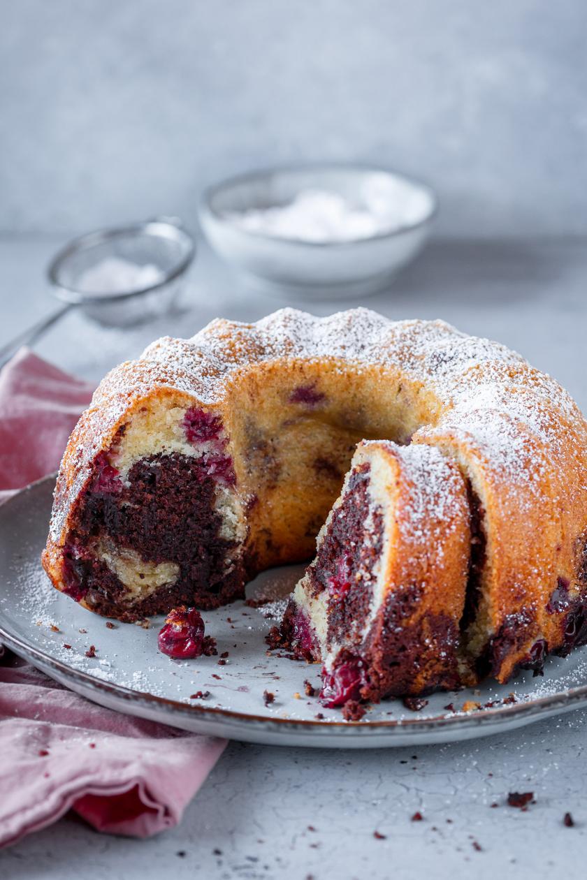 Angeschnittener Marmorkuchen mit Kirschen auf Tortenplatte.