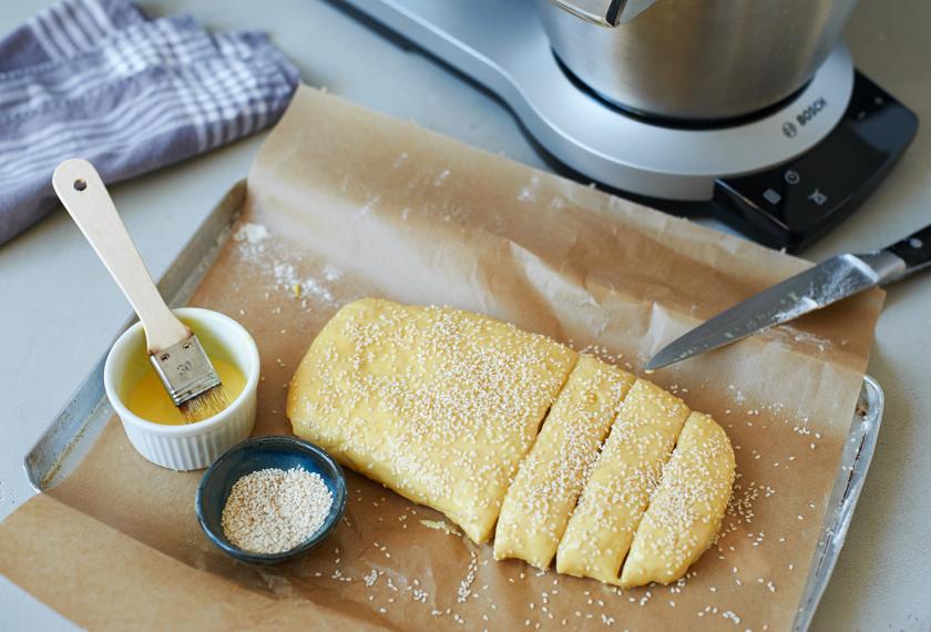 Der Teig für Milchbrötchen liegt auf einem Backblech und ist mit Ei eingepinselt.