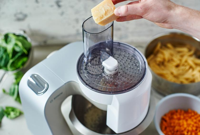 Für den Nudelauflauf mit Kürbis und Spinat wird Parmesan in einer Küchenmaschine gerieben.