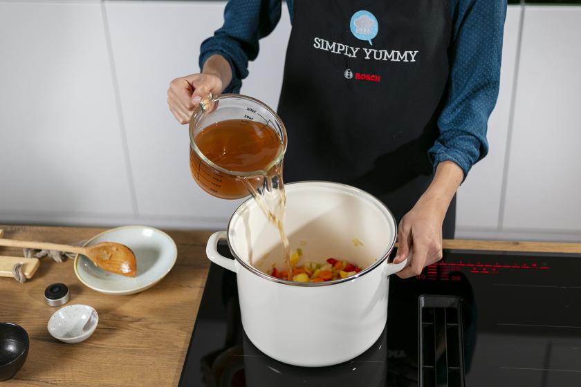 Omas Gemüsesuppe wird mit Brühe abgelöscht, die in den Topf zum Gemüse gegossen wird.