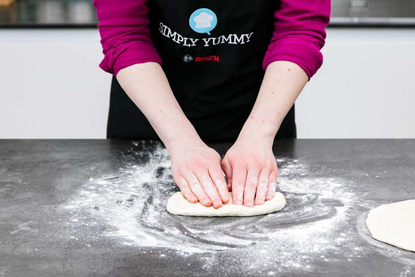 Der teig für Pizza Margherita wird mit den Händen flach gedrückt.