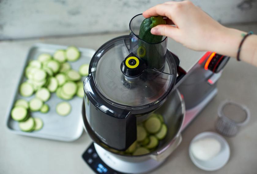 Für die Pizzaschnecken mit Pesto und Gemüse werden Zucchini mit einer Küchenmaschine in Scheiben gehobelt.