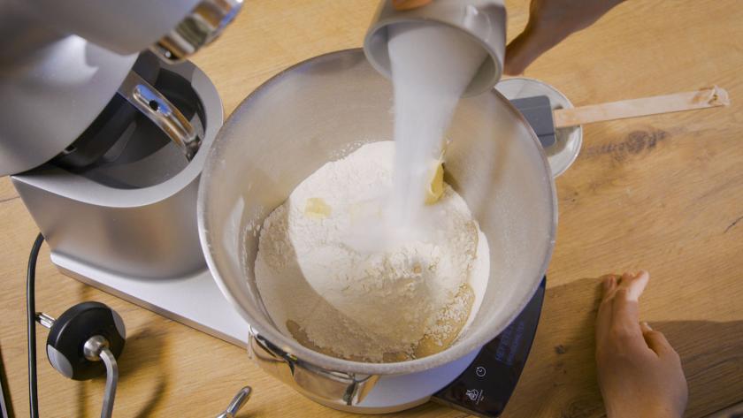 Zucker wird zu den Teigzutaten in die Rührschüssel einer Küchenmaschine gegeben.