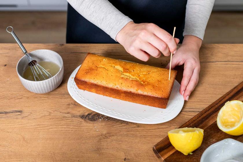 Zitronenkuchen wird mit einem Holzstäbchen mehrfach eingestochen.