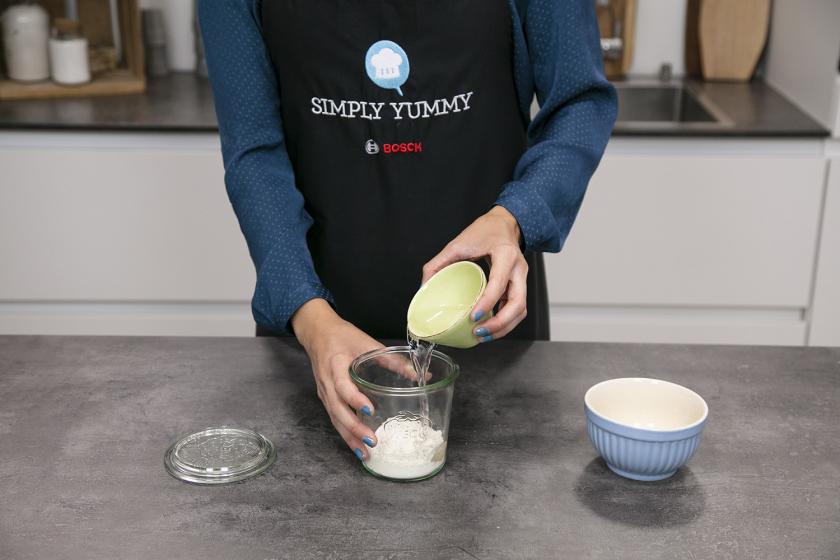 Für das Sauerteigbrot wird Wasser zu Mehl in ein Glas gegeben.