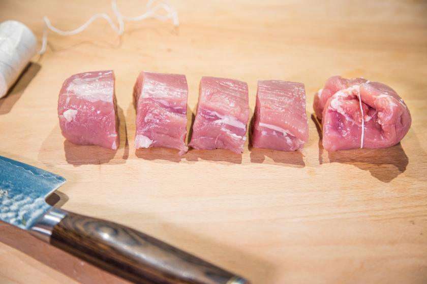 Fleisch liegt auf einem Brett und ist in Schweinemedaillons geschnitten.