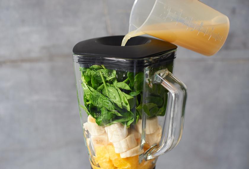 Für doe Smoothie Bowl mit Bananen wird Saft in den gefüllten Mixer gegossen.