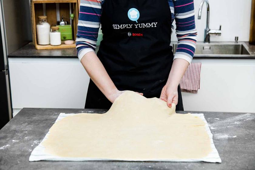 Der Strudelteig wird mit den Handrücken vom Küchentuch aufgenommen.