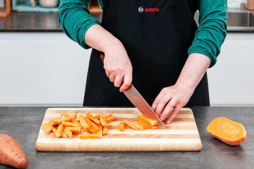 Süßkartoffel wird auf einem Brett in Süßkartoffel-Pommes geschnitten.
