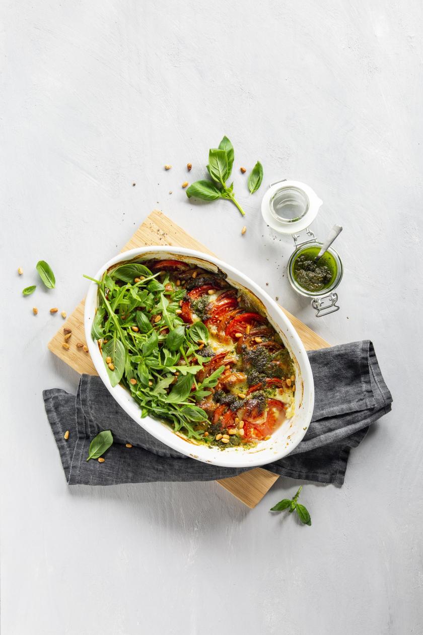 Tomate-Mozzarella-Auflauf mit Rucola in weißer Auflaufform.