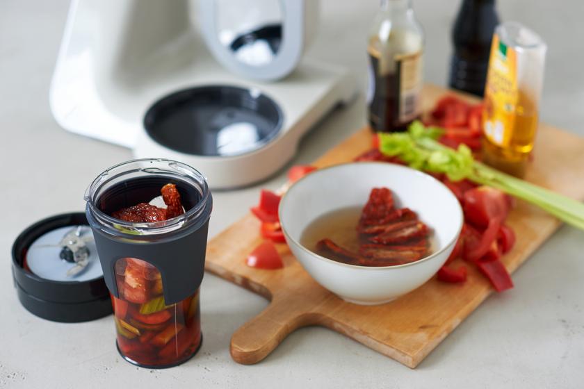 Die Zutaten für den Tomatensmoothie werden in einem Mixer püriert. Daneben Zutaten auf einem Holzbrett.