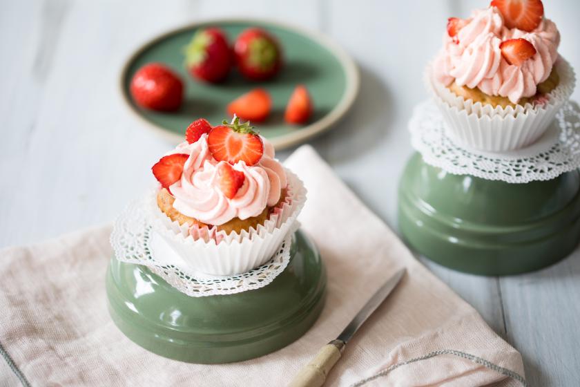 Vegane Erdbeercupcakes mit Frostig und frischen Erdbeeren auf einer umgedrehten Schale serviert.