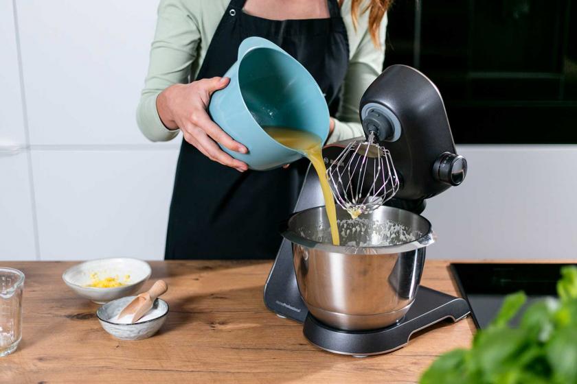 Orangensaft wird zum Teig für den Zitronenkuchen vom Blech in die Rührschüssel der Küchenmaschine gegeben.