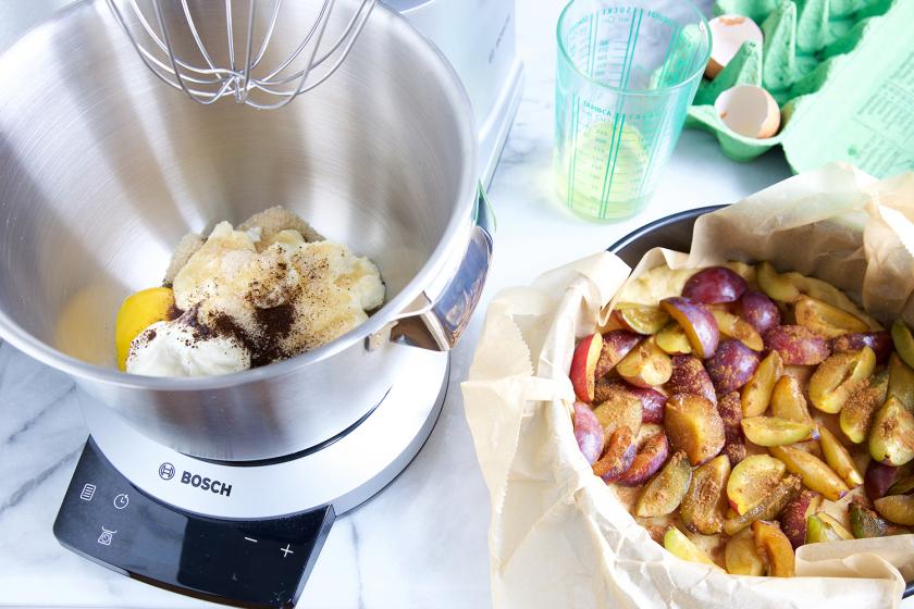 Die Füllung für den Zwetschgen-Quark-Kuchen wird in einer Küchenmmaschine zubereitet. Daneben geschnittene Zwetschgen.