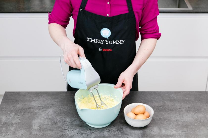 Eier und Zucker werden in einer Rührschüssel mit einem Handmixer für den Regenbogenkuchen aufgeschlagen.