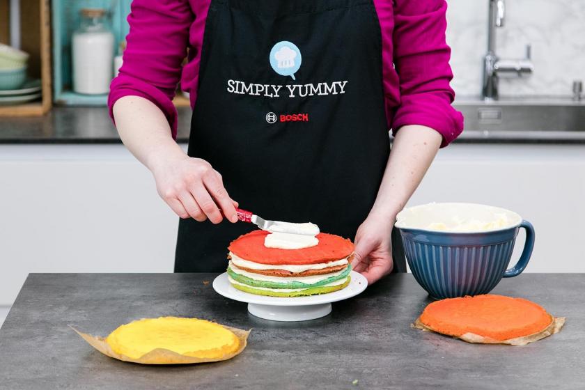 Ein Boden des Regenbogenkuchens wird mit Creme eingestrichen.