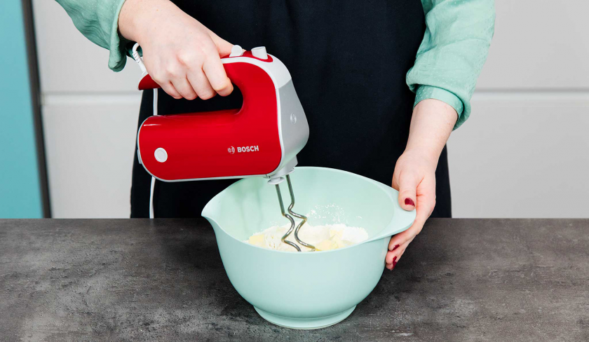 Die Zutaten für den Boden des Rhabarberkuchens mit Quark werden in einer Schüssel mit einem Handrührer geknetet.
