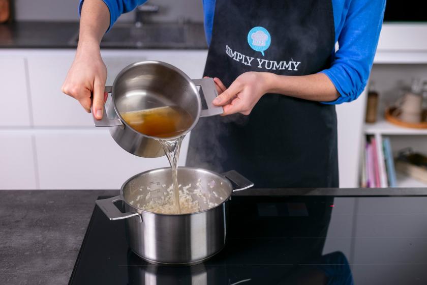Brühe wird in den Topf mit Risotto gegeben.