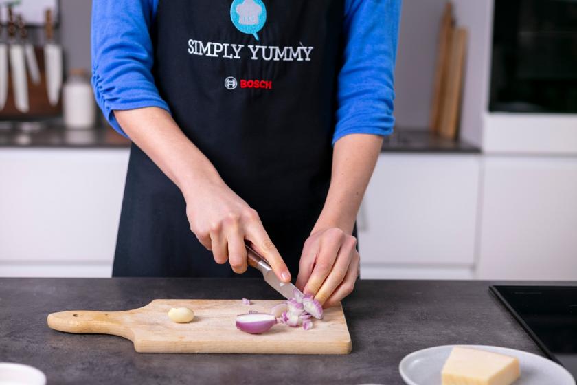 Zwiebel wird auf einem Holzbrett gewürfelt.
