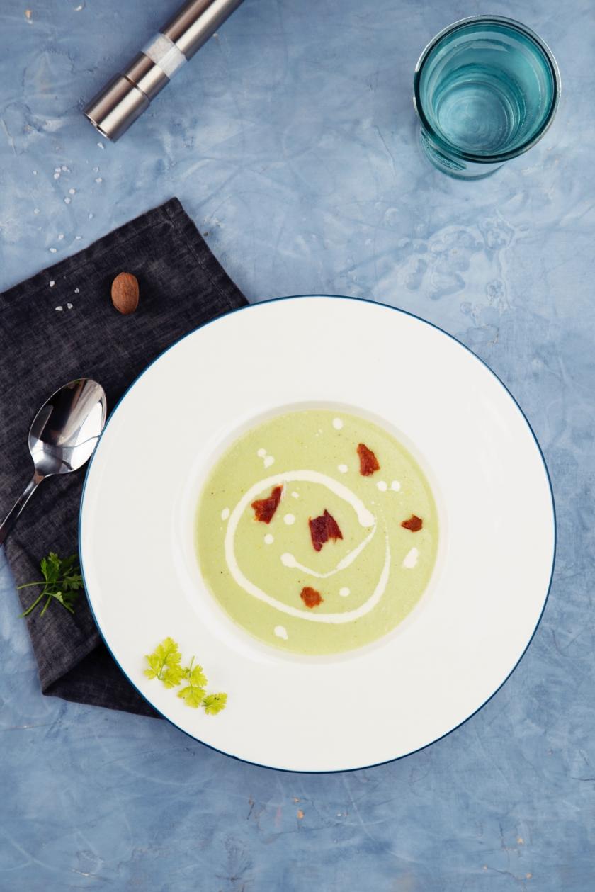 Rosenkohlcremesuppe in weißem Teller auf blauem Tisch