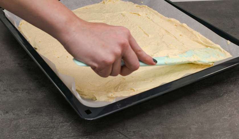 Für die Schmandschnitten mit Glühweinkirschen wird Teig auf einem Backblech glatt gestrichen.