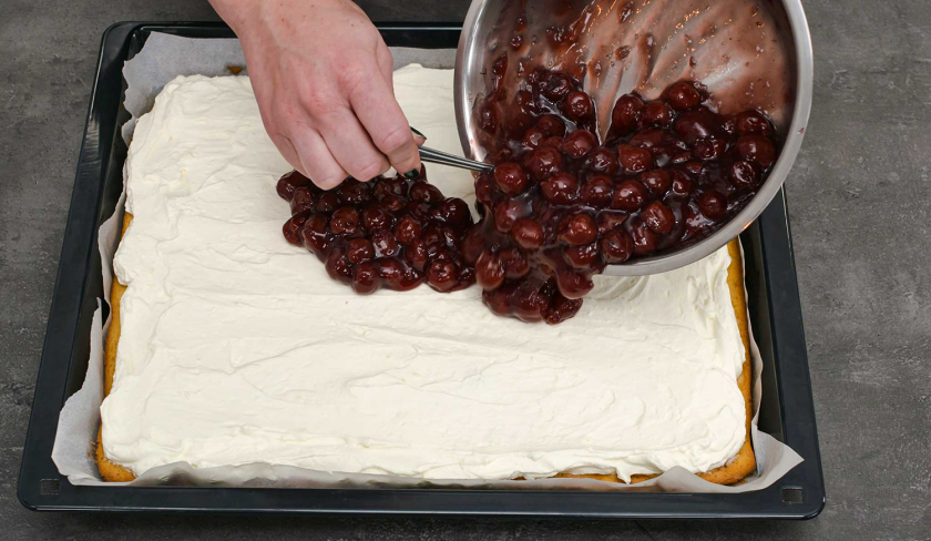 Für die Schmandschnitten mit Glühweinkirschen werden Kirschen auf der Schmandcreme verteilt.