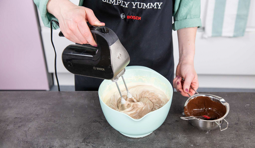 Die Füllung vom Schoko-Käsekuchen wird mit Schokolade in einer Schüssel und einem Handmixer verrührt.
