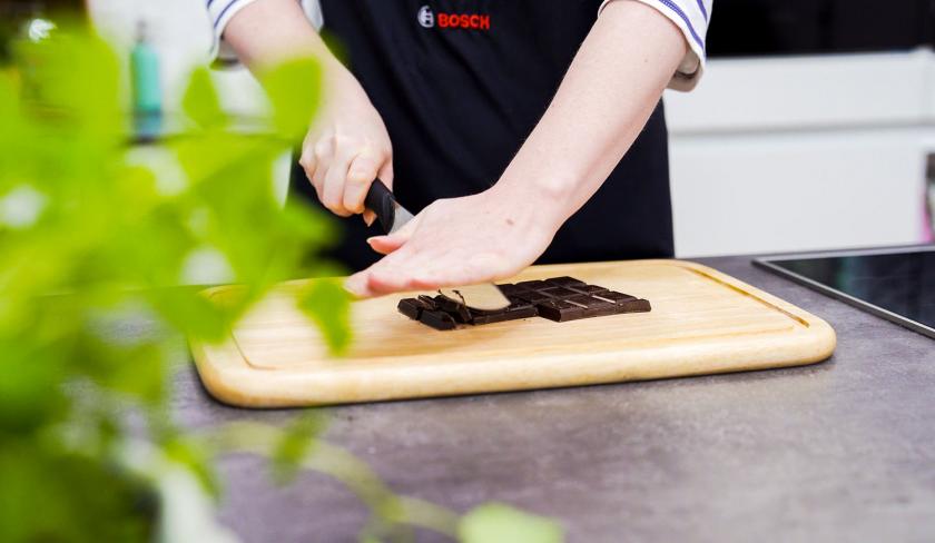 Für die Schoko-Kirsch-Muffins wird Schokolade auf einem Holzbrett gehackt.
