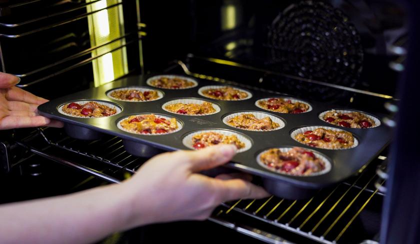 Ein Blech mit Schoko-Kirsch-Muffins wird in den Backofen geschoben.