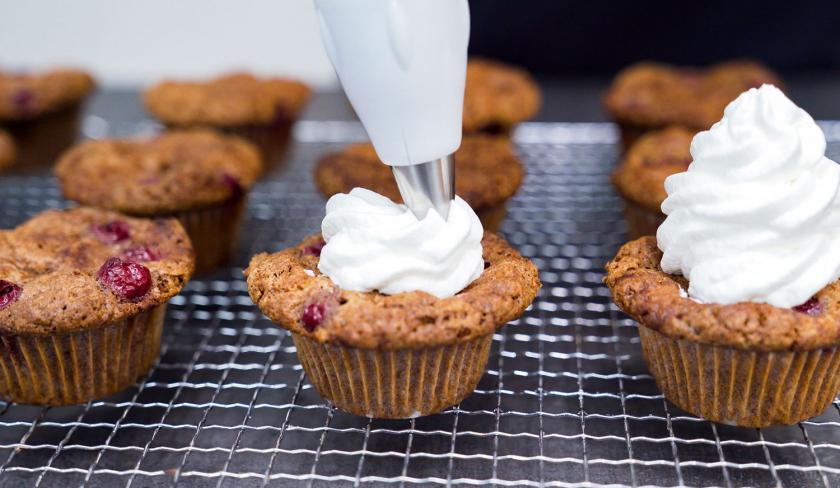 Die Schaumkussmasse wird mithilfe eines Spritzbeutels auf die Schoko-Kirsch-Muffins gespritzt.