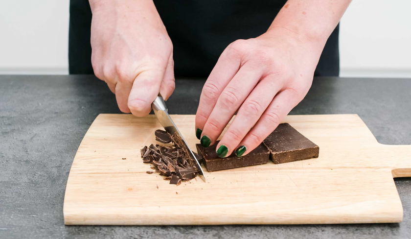 Für den Schoko-Nusskuchen mit Cheesecake-Frosting wird Schokolade gehackt.