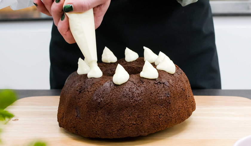 Es werden Frischkäsetupfen auf den Schoko-Nusskuchen mit Cheesecake-Frosting mit einer Spritztüte gesetzt.