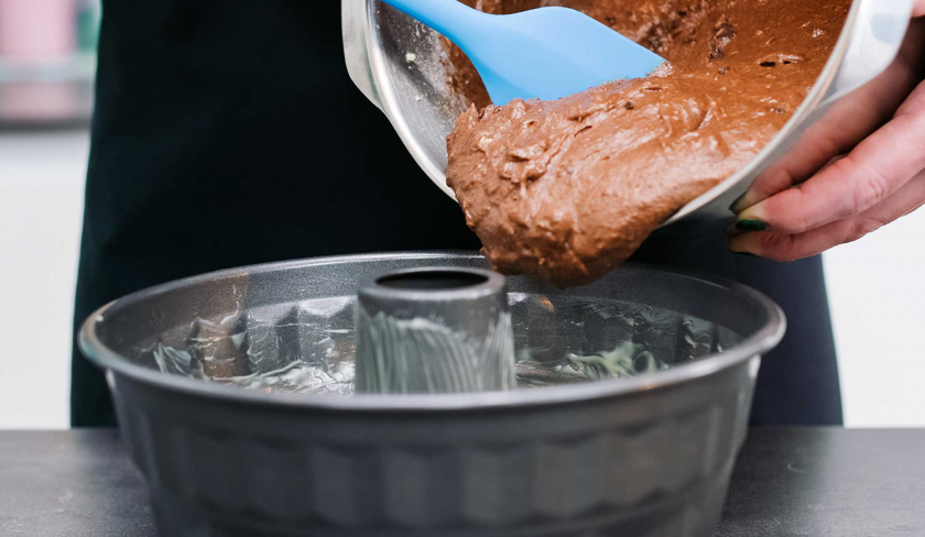 Der Teig des Schoko-Nusskuchen mit Cheesecake-Frosting wird in eine Gugelhupfform gegeben.
