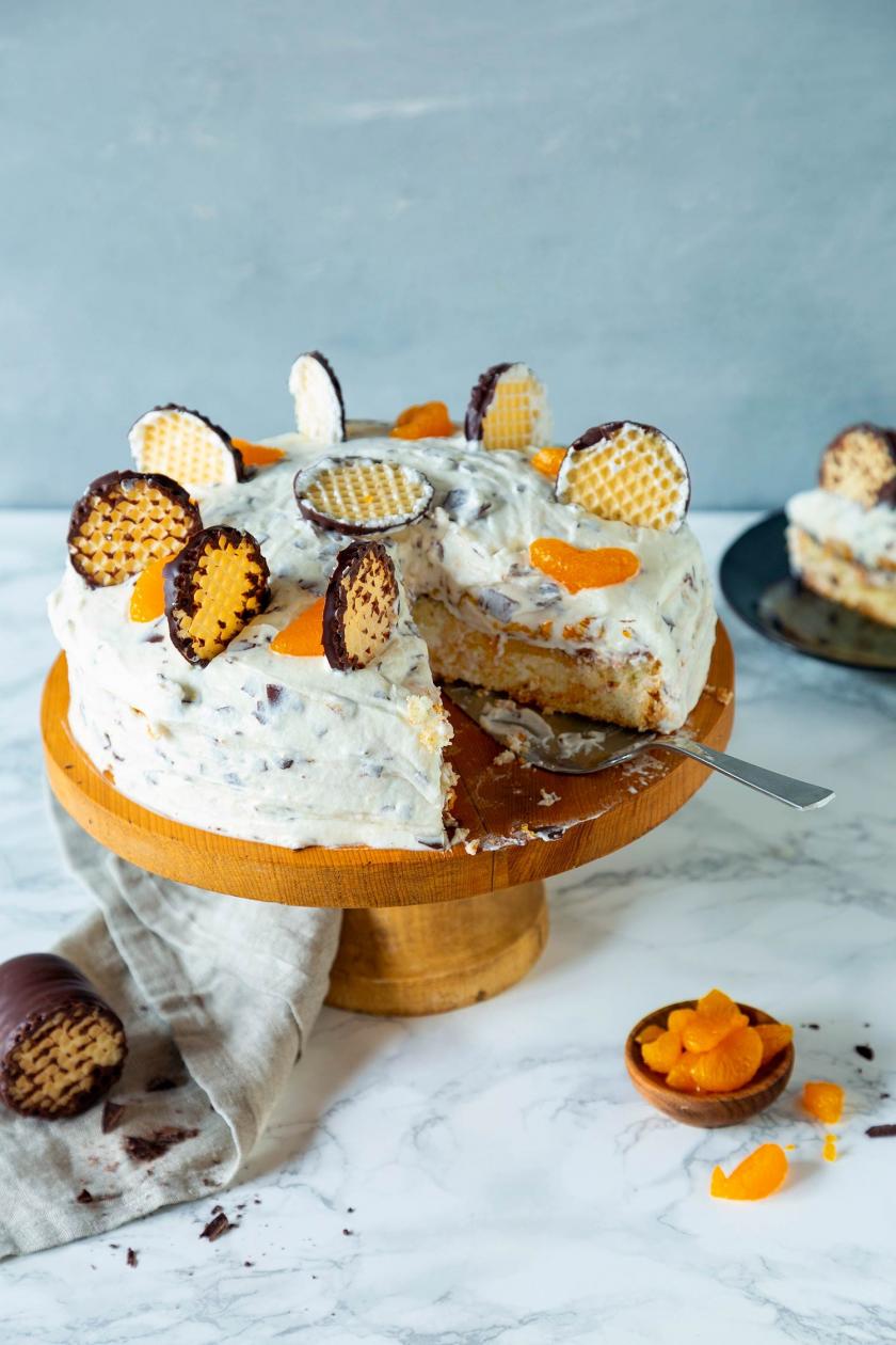 Schokokusstorte mit Mandarinen angeschnitten auf einer Kuchenplatte mit Kuchenheber.