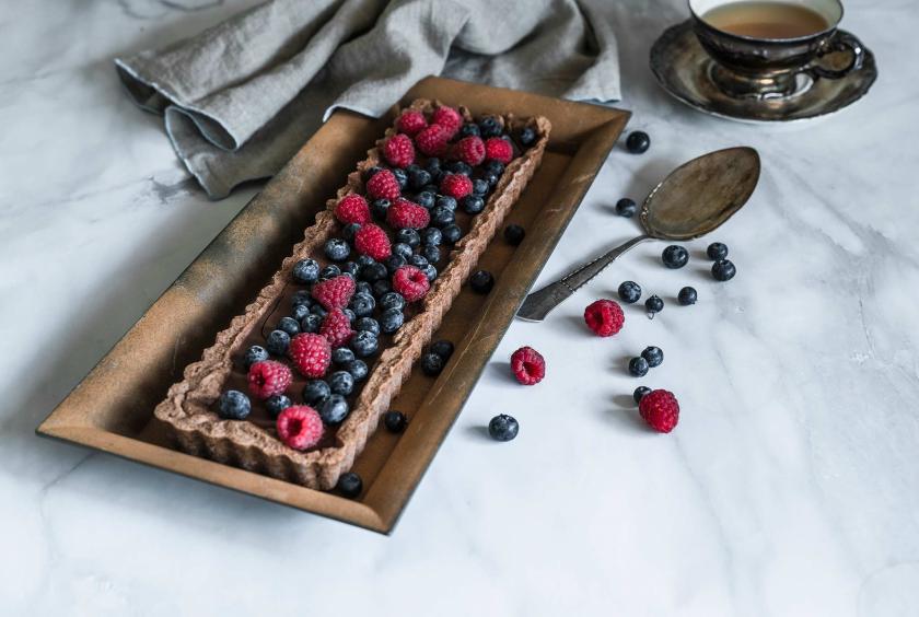 Eine Schokoladen-Tarte mit Beeren garniert liegt auf einem Kaffeetisch.