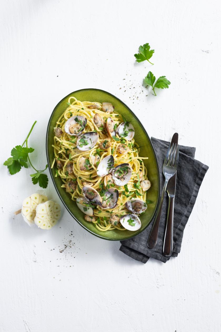 Spaghetti Vongole in einem Pastateller angerichtet mit Knoblauch und Petersilie.