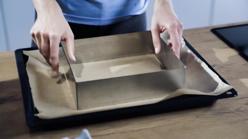 Ein Backrahmen wird auf einem Blech mit Backpapier positioniert.